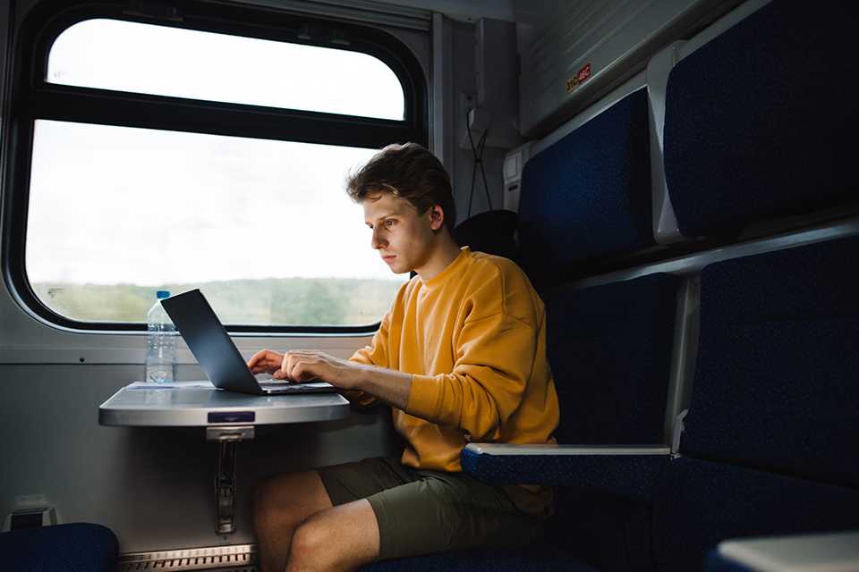 A man working on his laptop on the train while traveling.