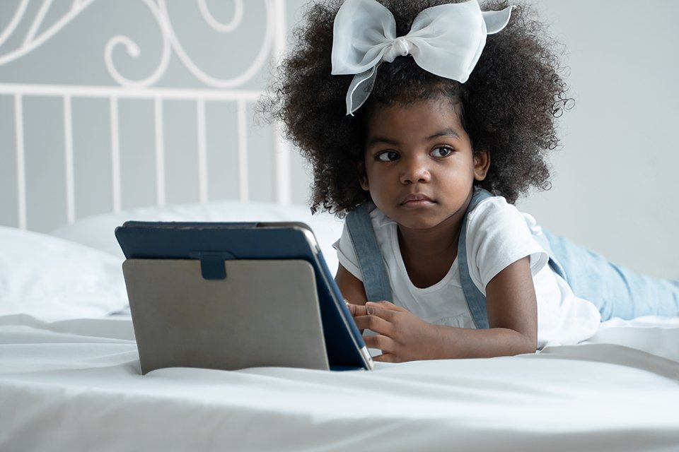  A kid lounging on her bed with a laptop open in front of her.