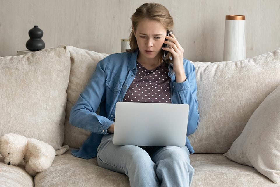 A woman working from home on her laptop while talking on the phone.