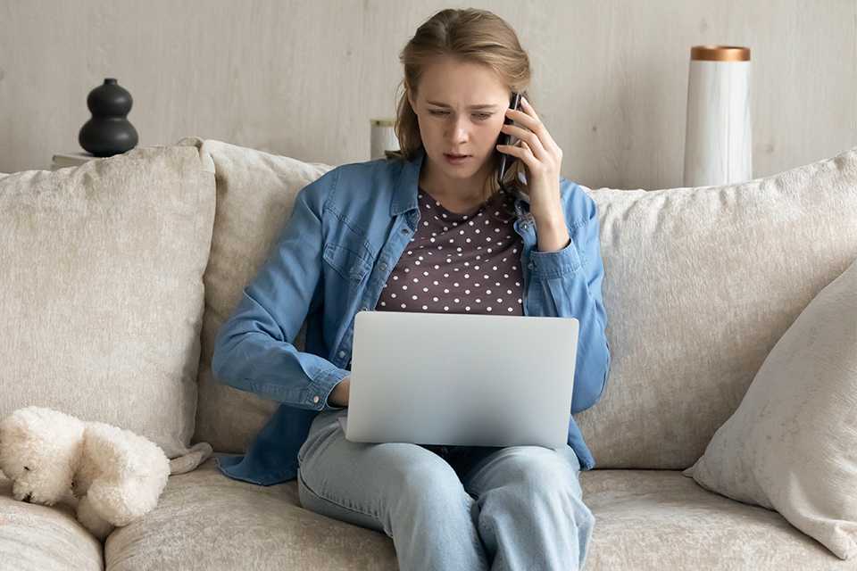 A woman working from home on her laptop while talking on the phone.