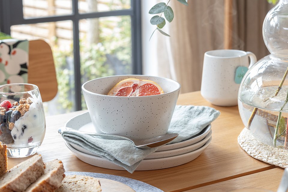 A Habitat white stoneware dinner set next to a glass vase on a wooden dining table.
