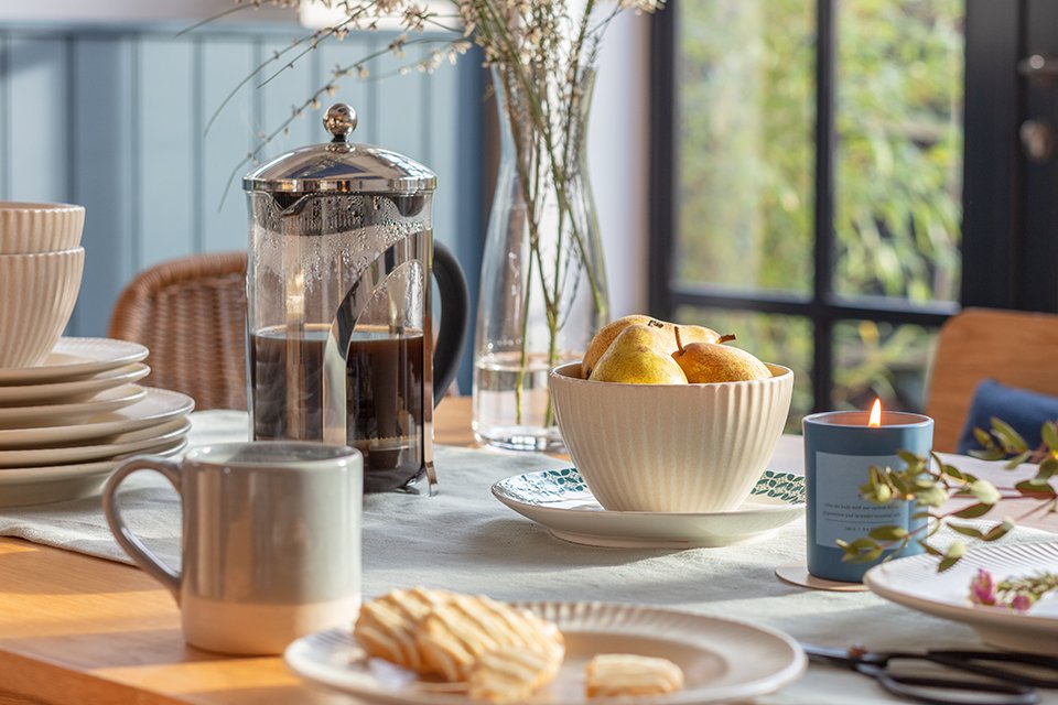 A Habitat stoneware dinner set in white displayed on a dining table along with a glass vase and a candle.
