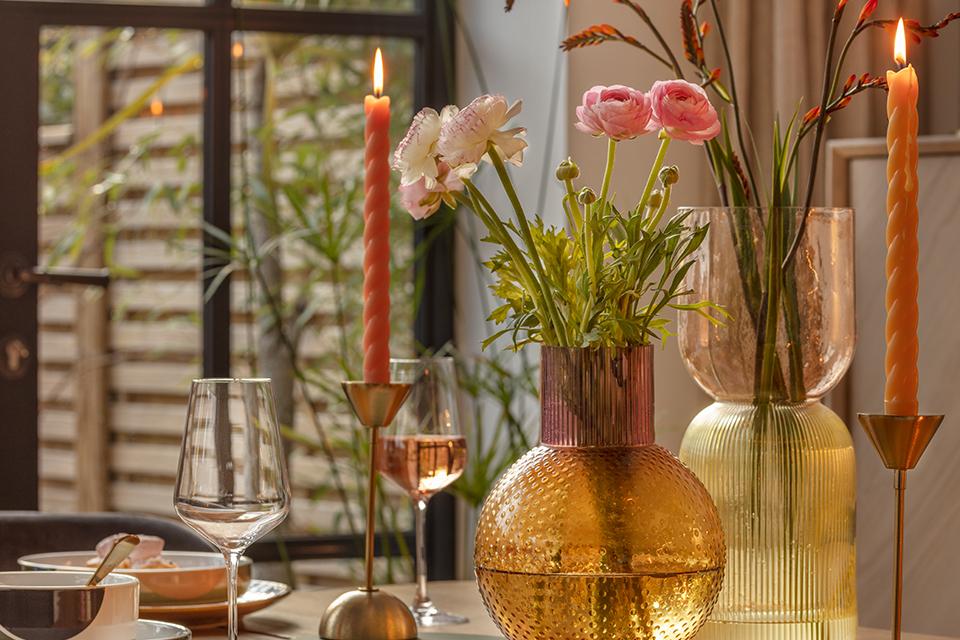 A dining table displaying gold and pink textured glass vases, candles and wine glasses. 