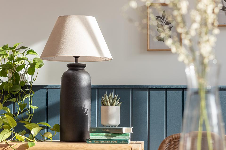 A Habitat tall ceramic table lamp in black with a white lamp shade next to an indoor succulent.