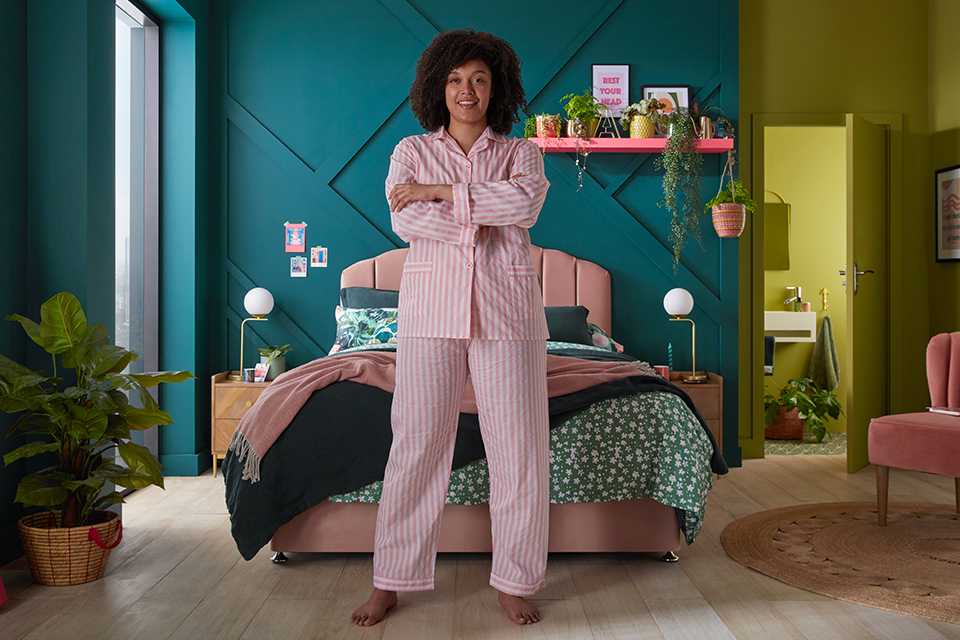 A woman in her pajamas, with her Silentnight bed, Eco mattress and lots of plants in the background.