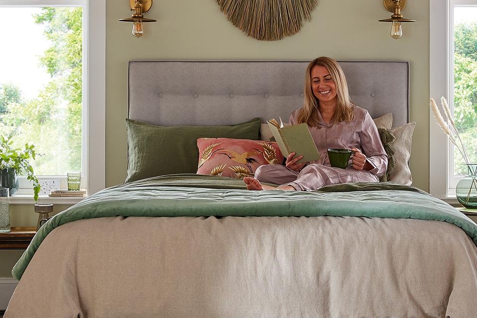 A woman curled up with a book and a cup, on her Silentnight Eco Breathe mattress.