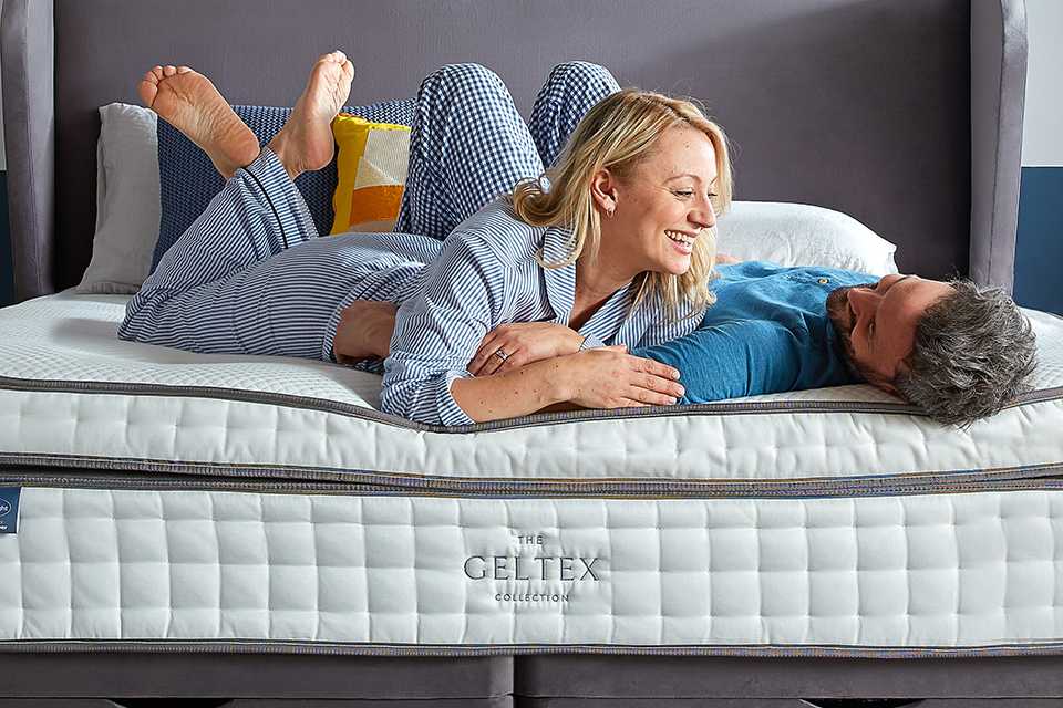 A playful couple in pajamas laughing, lying on the Silentnight Geltex mattress.