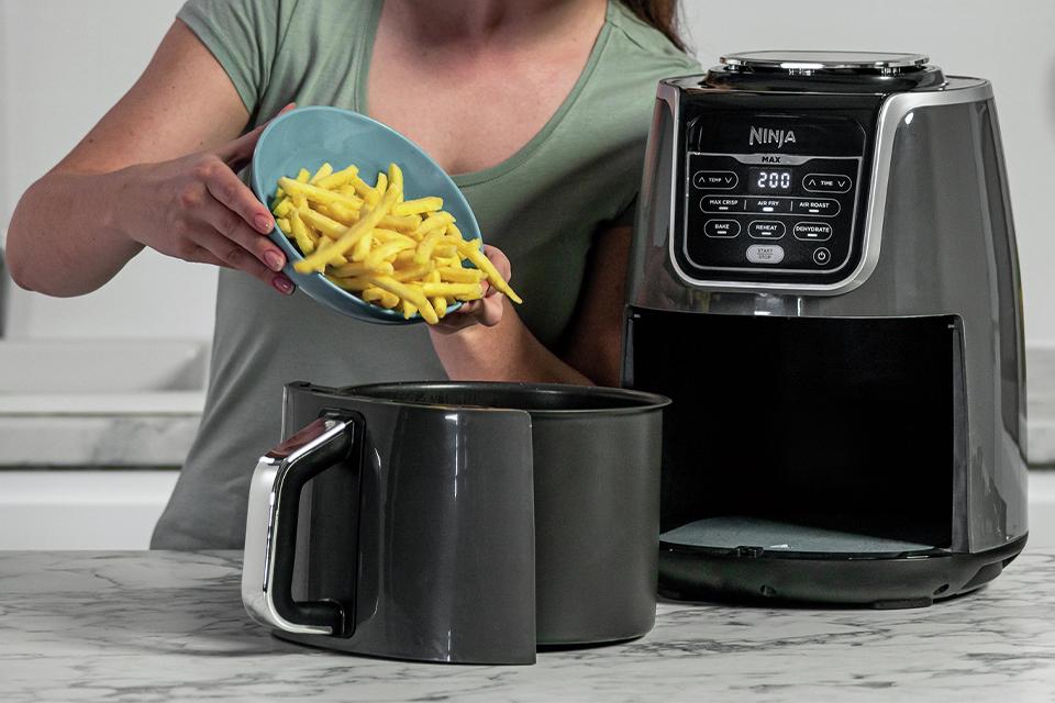 A woman pours chips into a Ninja air fryer.
