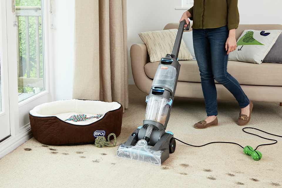 A woman using a Vax Dual power ECR2V1P pet advance carpet cleaner on a rug.