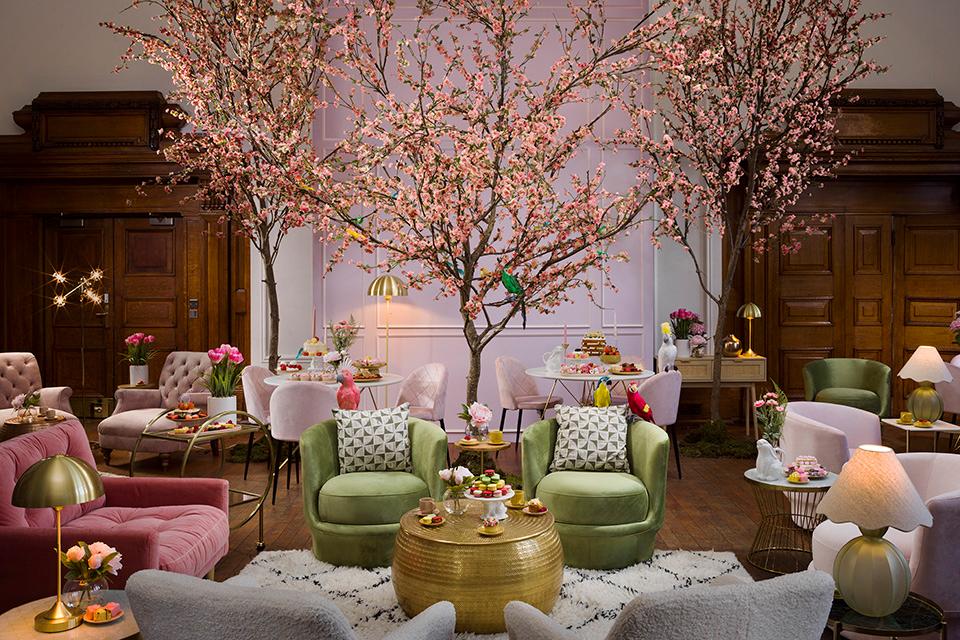 A tea party inspired room dotted with statement armchairs and table lamps with a faux cherry blossom tree at the centre. 