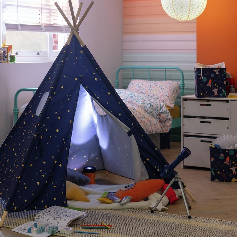 A kid's bedroom with a blue space print teepee, canvas storage boxes and metal framed bed with white bedding.