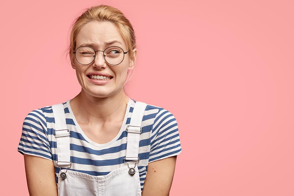 a nervous looking lady wearing dungarees and glasses