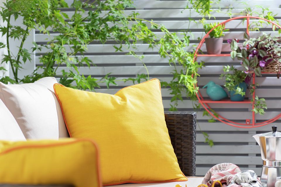 A close up image of a rattan effect garden sofa with yellow cushion on it. 