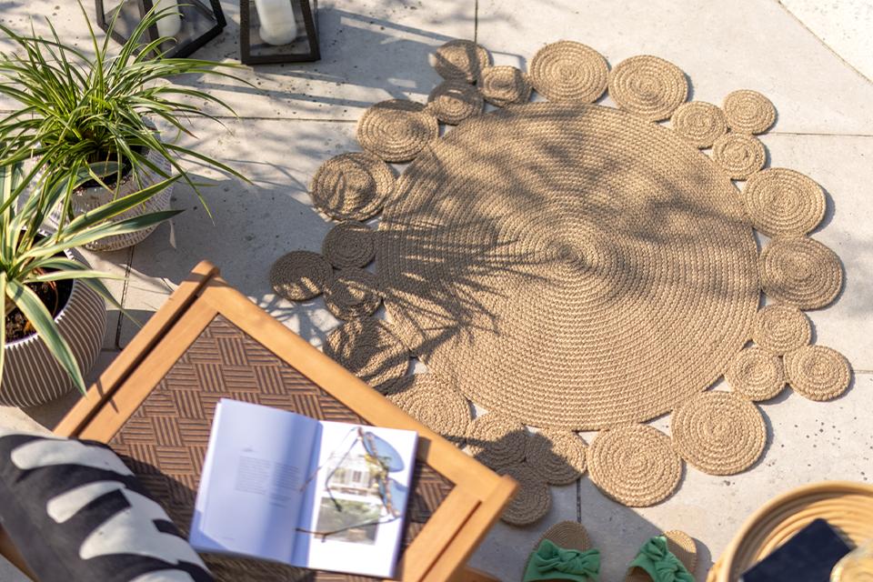 A Habitat round natural rug placed outdoors next to a wooden chair and side table.