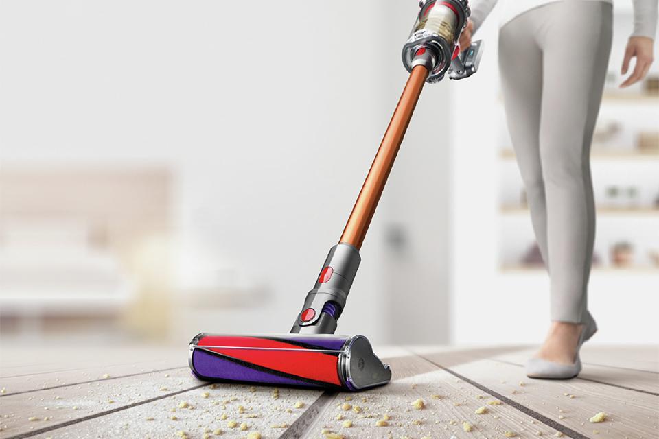 Woman vacuuming crumbs off of wooden floor with dyson cordless vacuum.