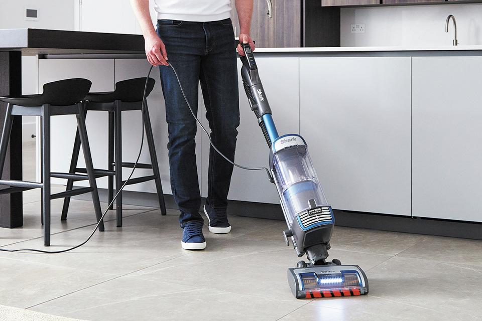Man vacuuming his kitchen floor with corded Shark upright vacuum.