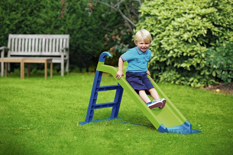 A toddler boy playing on a Chad Valley kid's garden slide in green and blue colour.