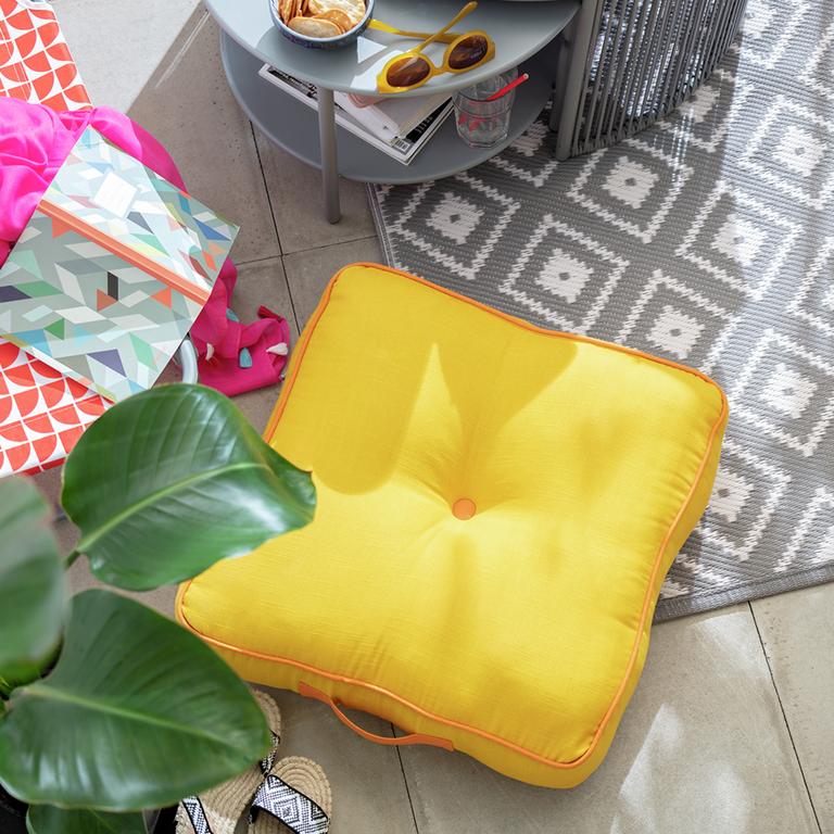 An outdoor floor cushion in bright mustard yellow colour placed on a grey rug. 