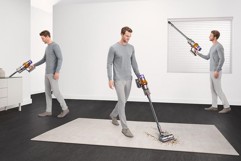 A man showing different functionalities of a Dyson cordless vacuum cleaner.
