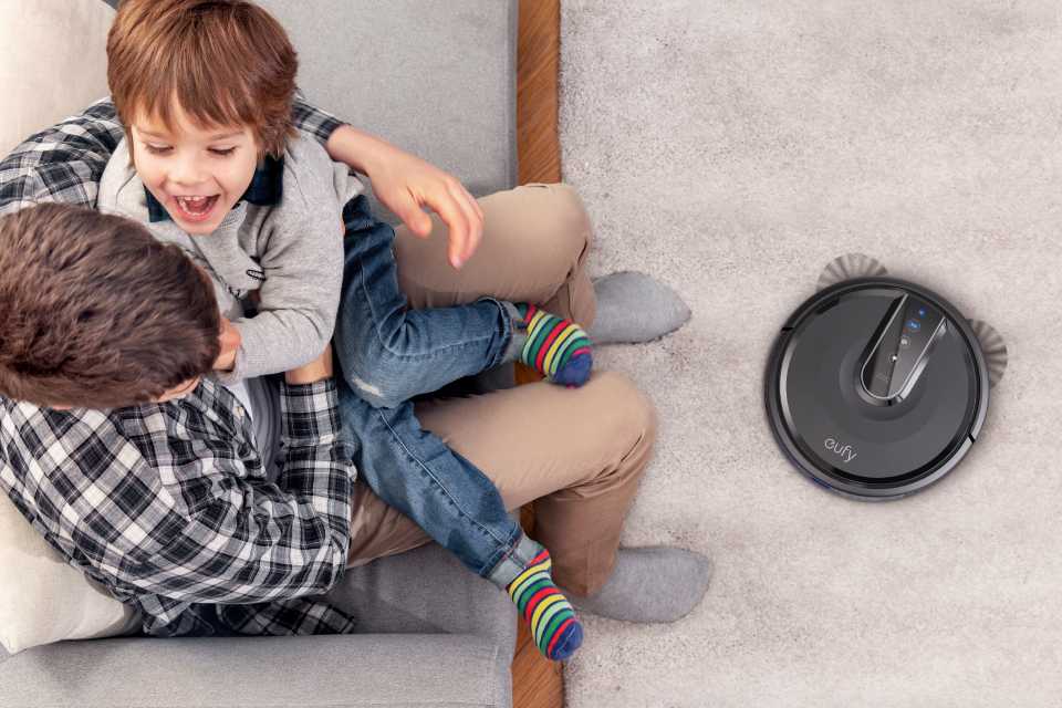 eufy RoboVac 35C gliding over the carpet and a father-son playing on the sofa.