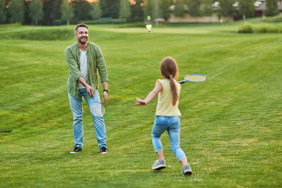 Father playing badminton with his little daughter outdoors.