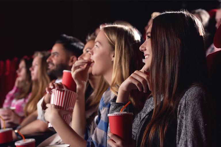 A group of friends watching a movie at a theater while having popcorn.