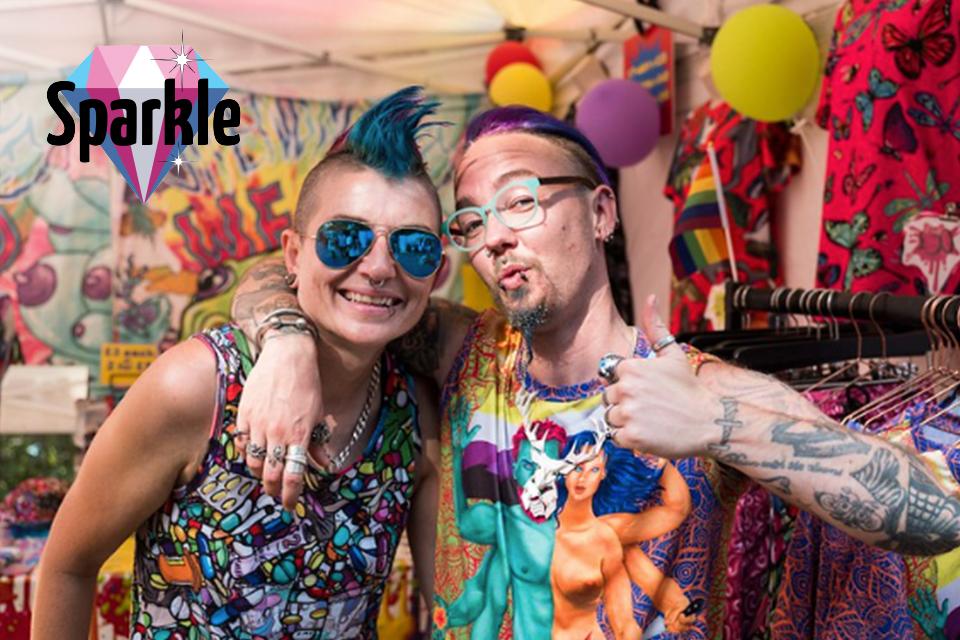 2 people with brightly coloured hair and tattoos smile at the camera.