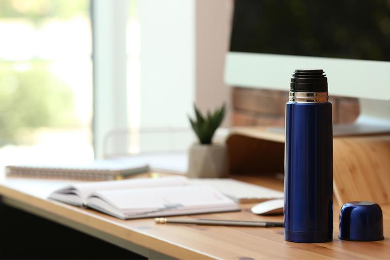 A modern thermos on wooden desk at workplace.