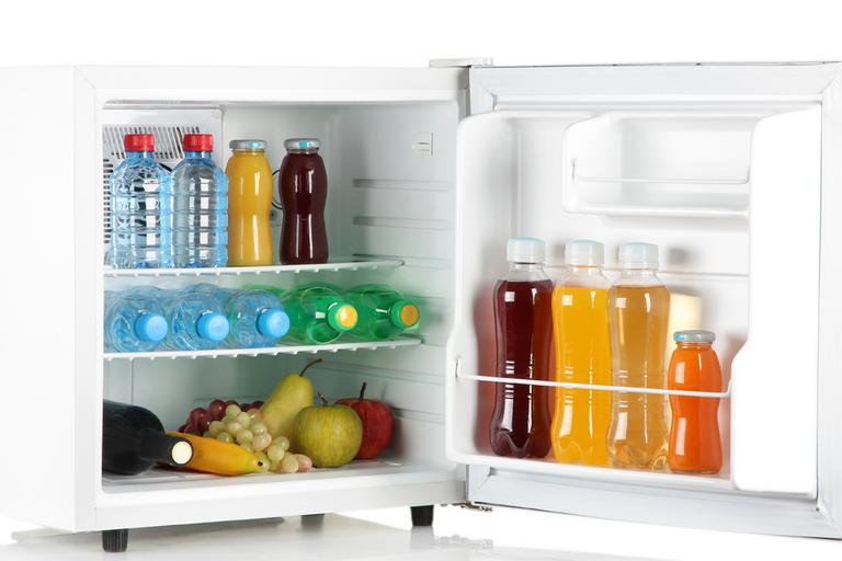 A mini fridge full of bottles of juice, soda and fruit.