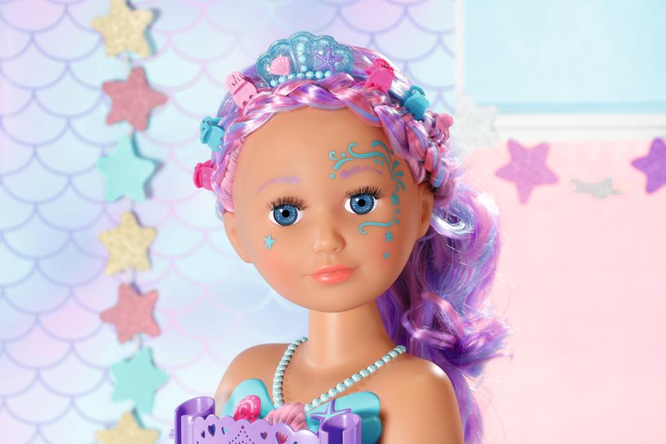 A BABY born Styling Heads doll with long colourful hair, a blue crown, and a face tattoo.