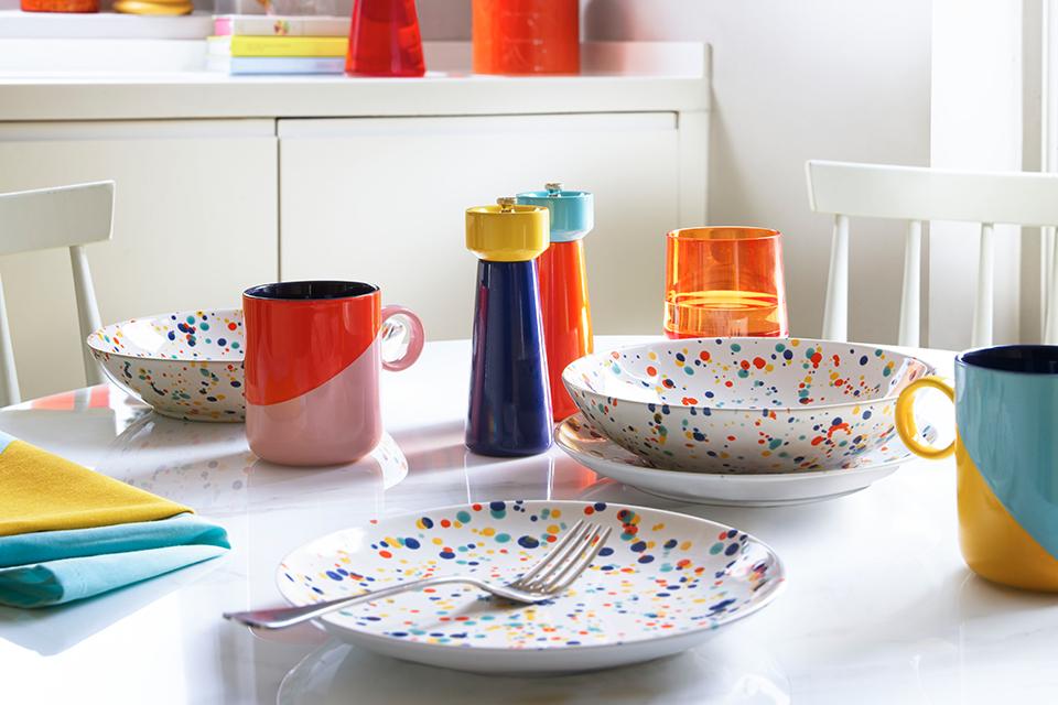 A white kitchen with multi-colour theme displaying a white dining table, colourful salt and pepper set, cookware and dinner set. 