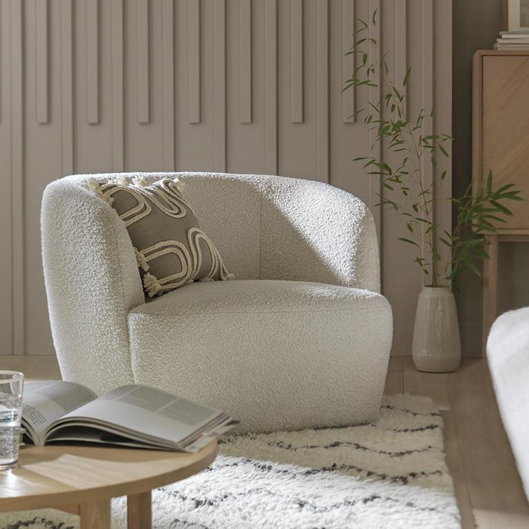 A Habitat boucle armchair in white paired with a white boucle sofa and woolen rug. 
