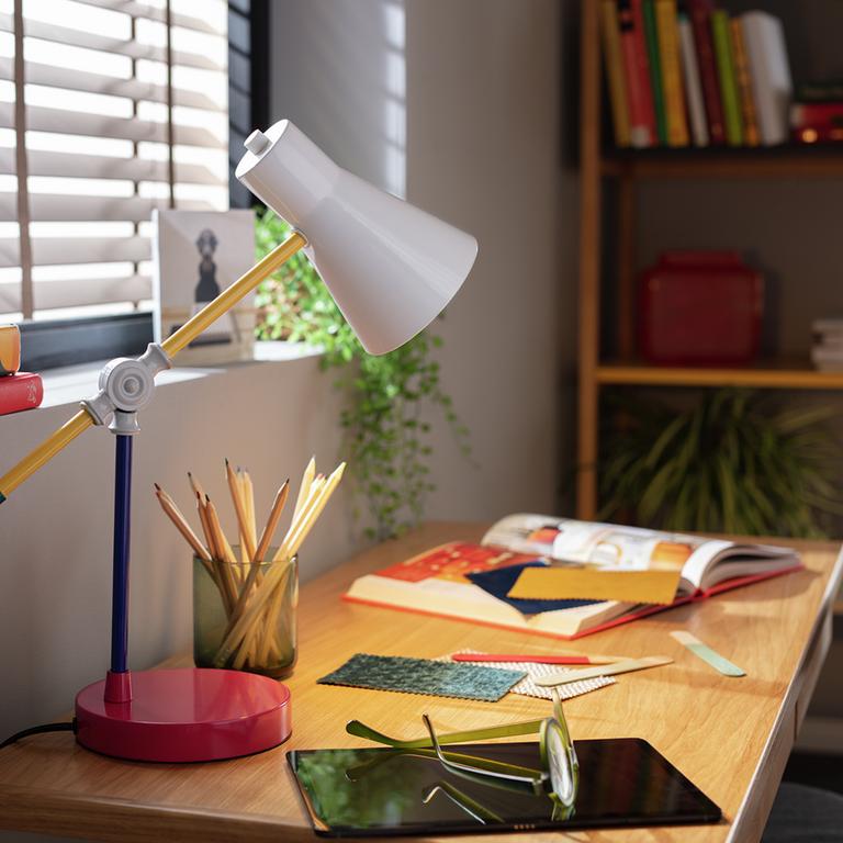 A Habitat colour block desk lamp in yellow, white, pink and green placed on a desk next to a window.  