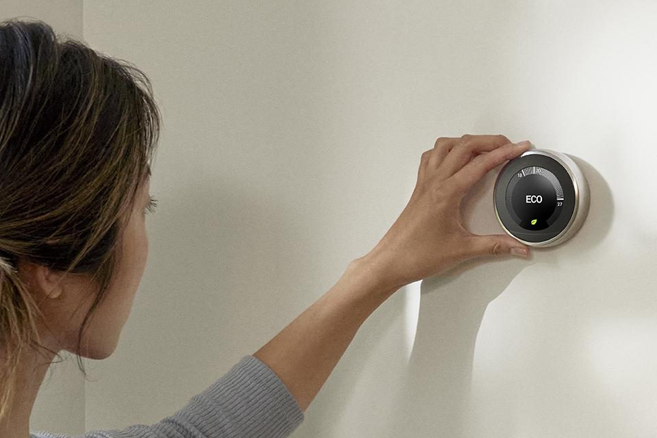A woman adjusting a Google Nest Learning thermostat.