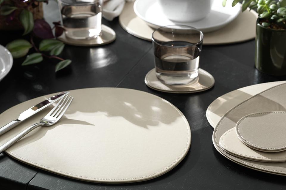 A set of 4 Habitat faux leather pebble placemats and coasters on a black dining table.