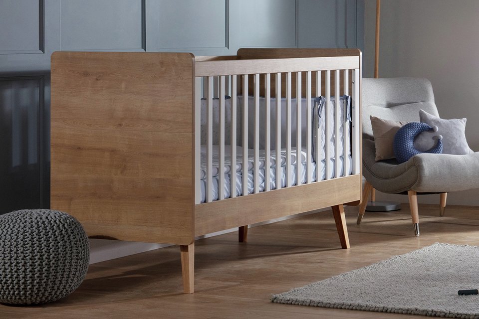 A wooden Silver Cross Westport cot bed placed in a living room.