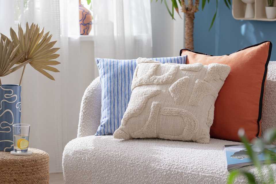 A Habitat tufed cotton cushion in cream colour on a boucle while sofa. 