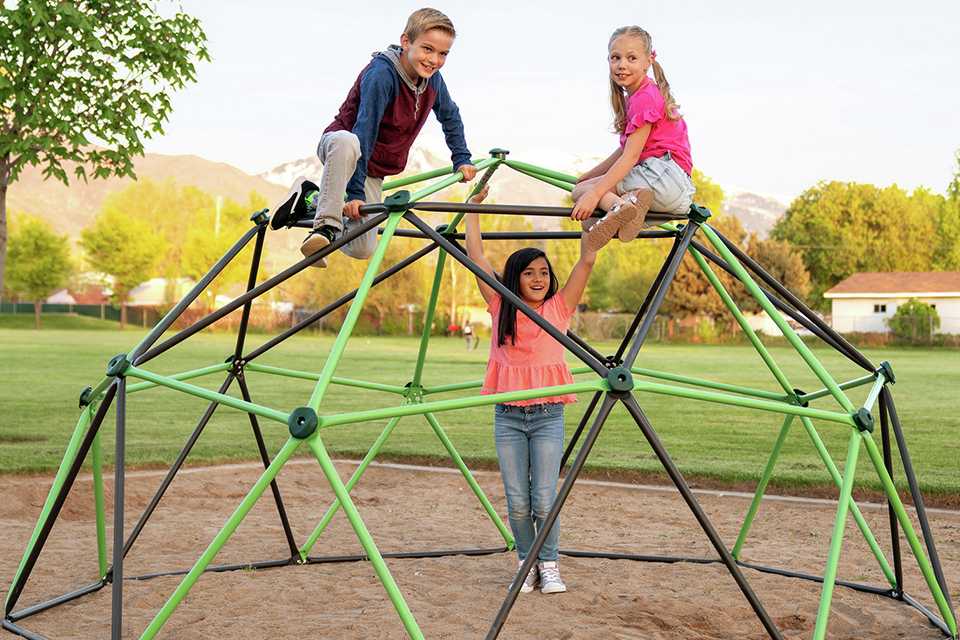 3 kids on a dome climber in a lawn.