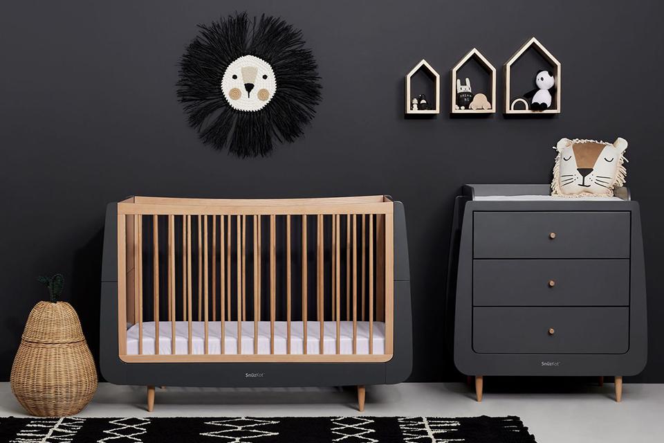 A Snuz Kot skandi cot bed in slate and natural finish beside a matching chest of drawers in a kid's room. 