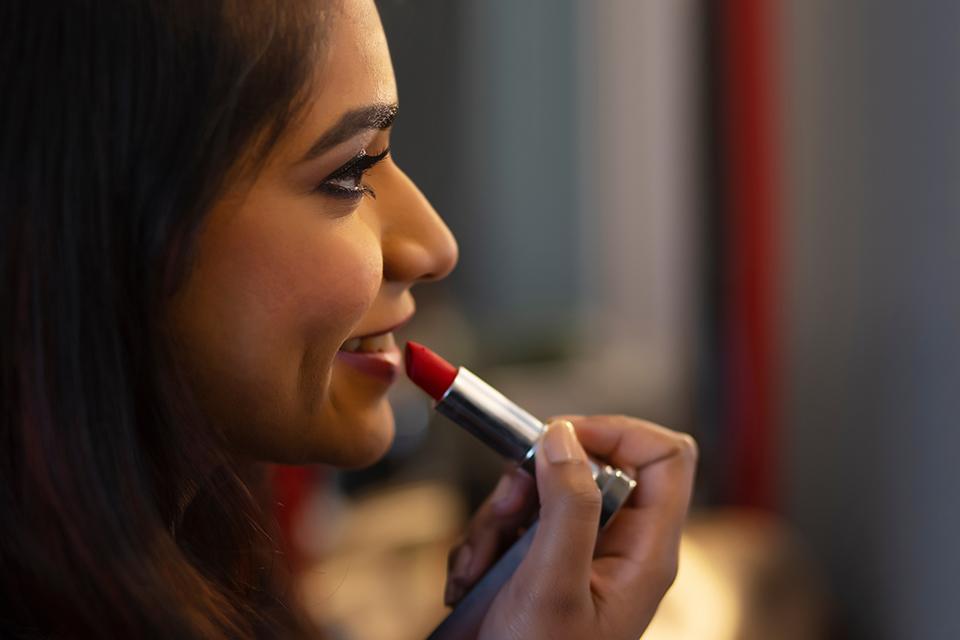 Close-up portrait of a young woman applying red lipstick.