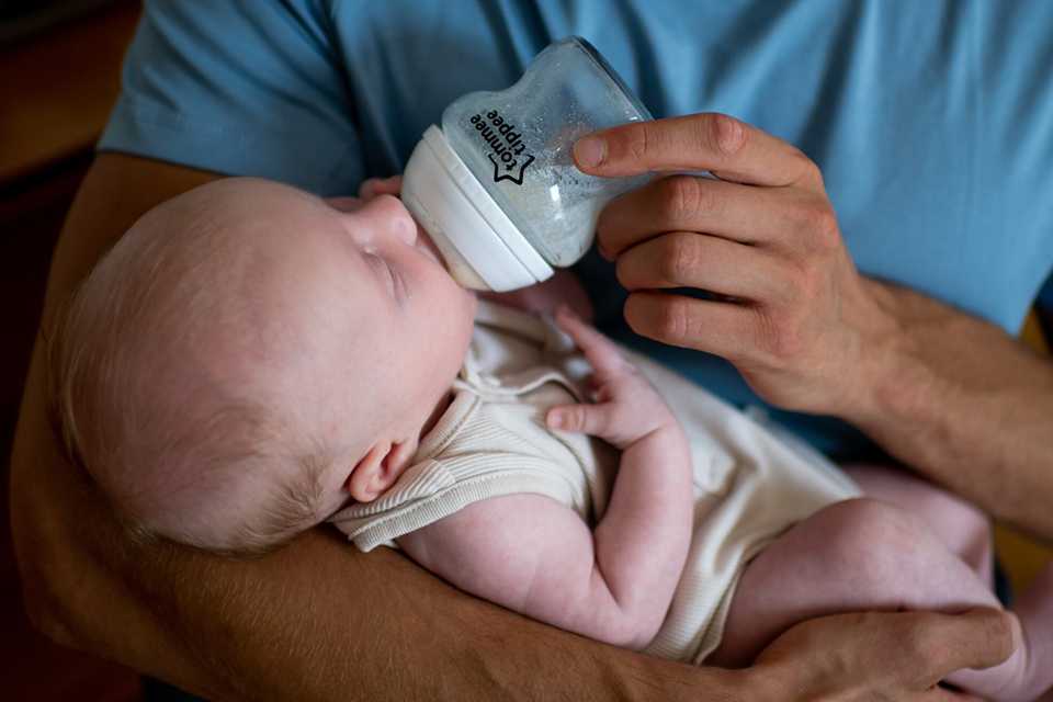 A father feeding his baby using a Tommee Tippee bottle.