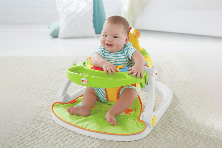 A baby sitting on a Fisher-price giraffe sit me up feeding booster seat in green colour.