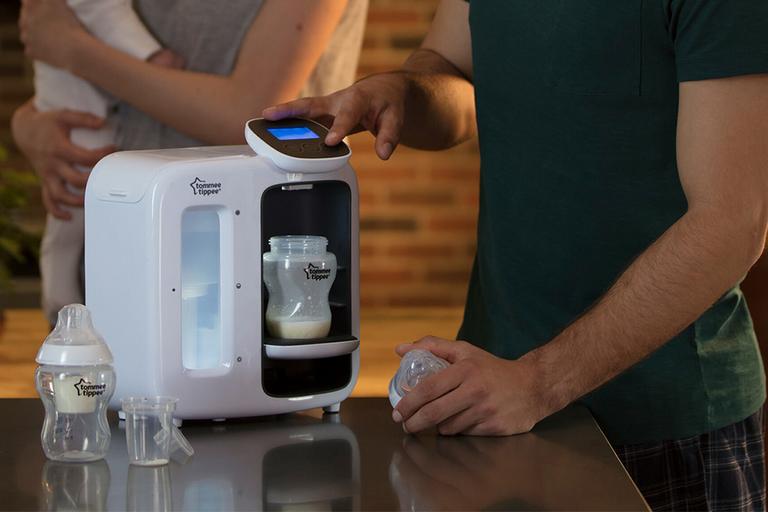 A father using a Tommee Tippee perfect prep day and night machine to prepare a bottle while the mother holds the baby.