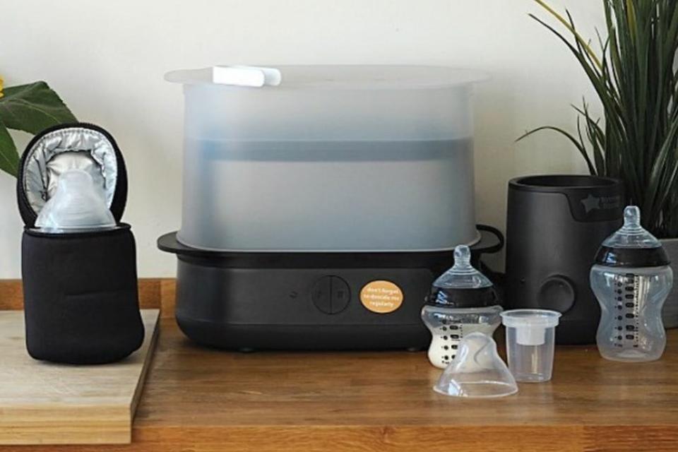 A Tommee Tippee complete feeding set with a bottle steriliser in black colour placed on a wooden kitchen worktop.