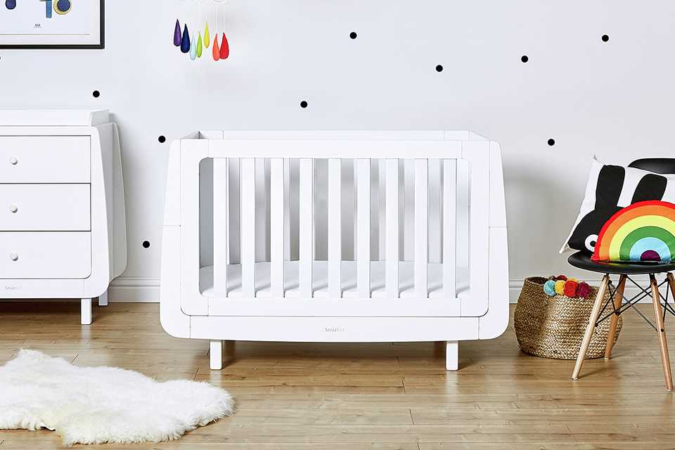 A white cot and a changing table kept in a nursery.