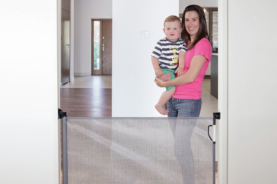 A woman and a baby standing next to a Dreambaby retractable tall safety gate.