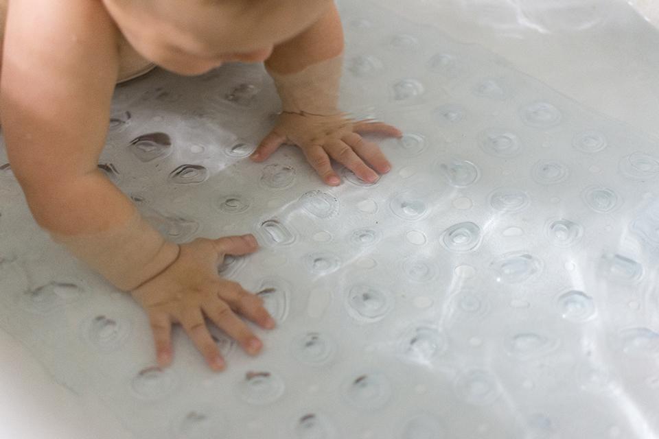 Young baby on a clear bath mat with suction cups used to prevent slipping.
