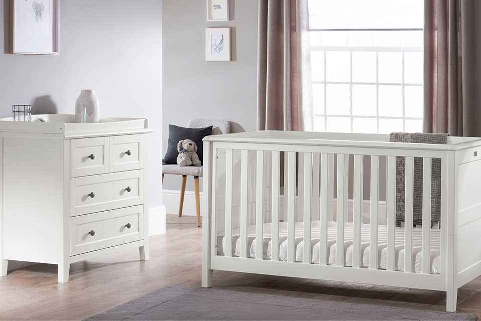A white nursery set with cot and chest in a nursery.