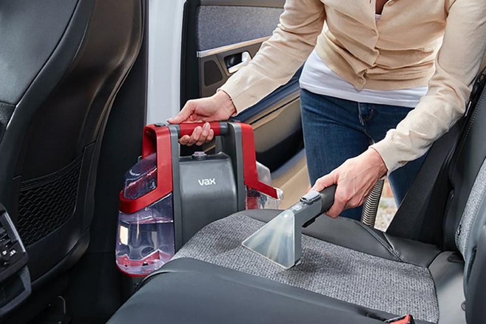 a woman cleaning car seats with a Vax spot washer.