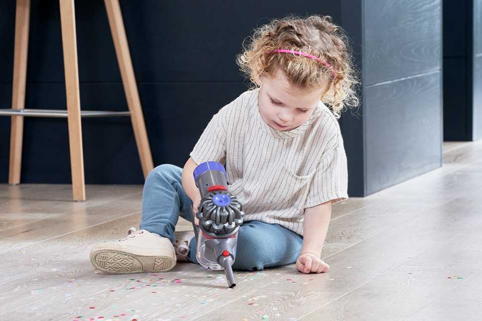 A toddler using Dyson Cordless toy vacuum cleaner on the floor.
